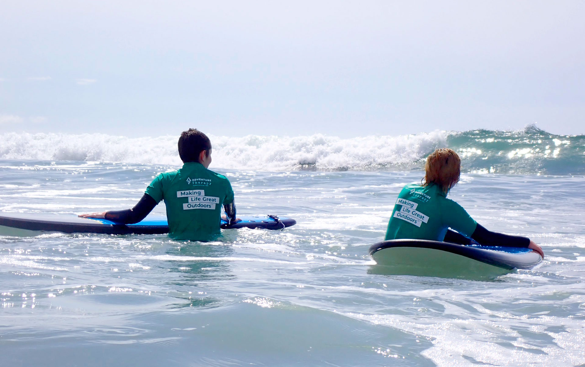 Two young people taking their boards out into the surf